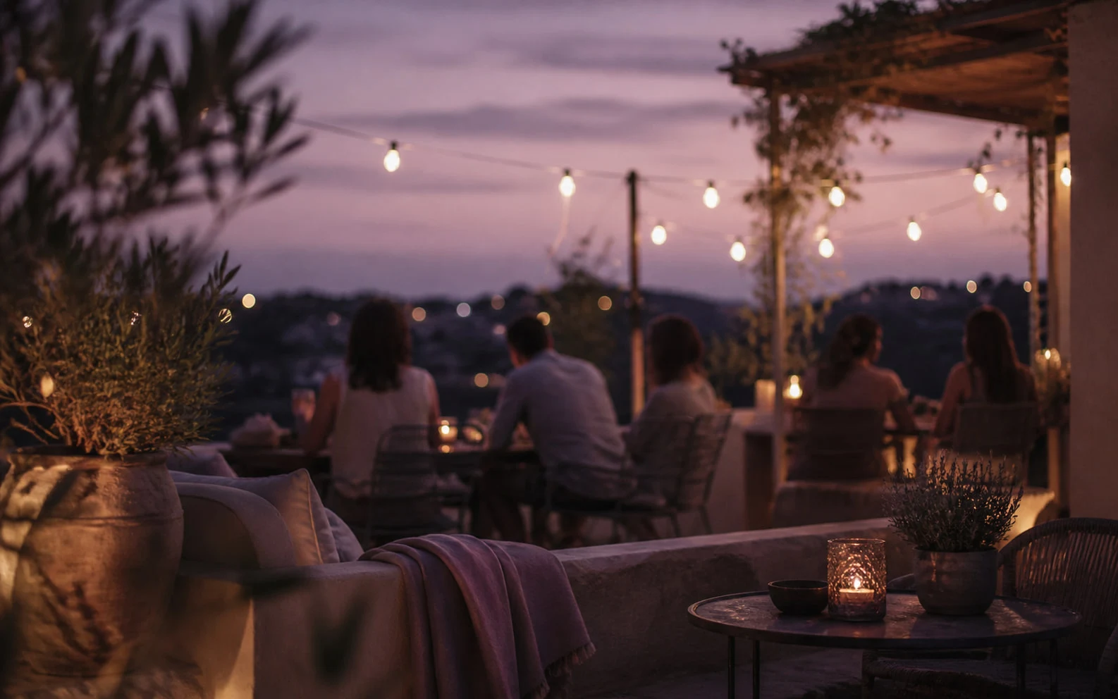 Terraza al anochecer con luces cálidas y varias personas conversando al fondo